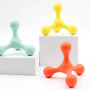 Three massage tools in teal, yellow, and orange sit on white platforms against a plain background.