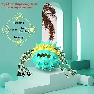 A blue and yellow spiky ball toy with ropes on a pedestal in a minimal room. Text lists its uses: teething, vocalizing, cleaning teeth, training.