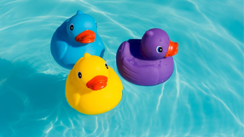 Three rubber ducks in purple, blue and yellow colors floating on water.