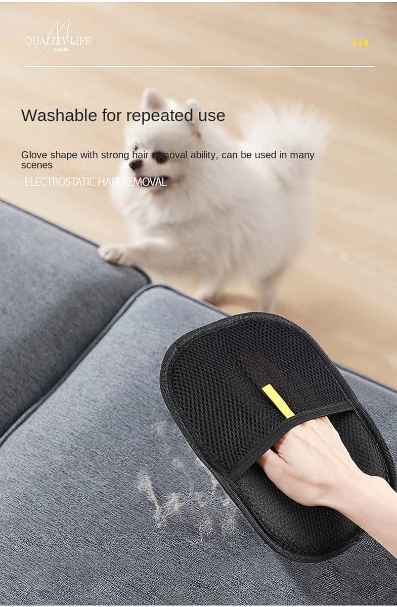 Eine Hand benutzt einen Handschuh zur Tierhaarentfernung auf einem grauen Sofa, während ein kleiner weißer Hund daneben auf dem Holzboden sitzt.
