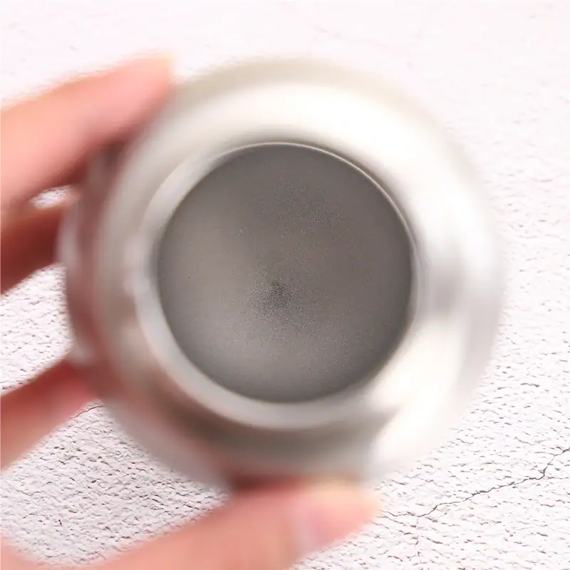 Close-up view of a stainless steel travel mug held by hand, showing the open lid and interior, against a textured white background.