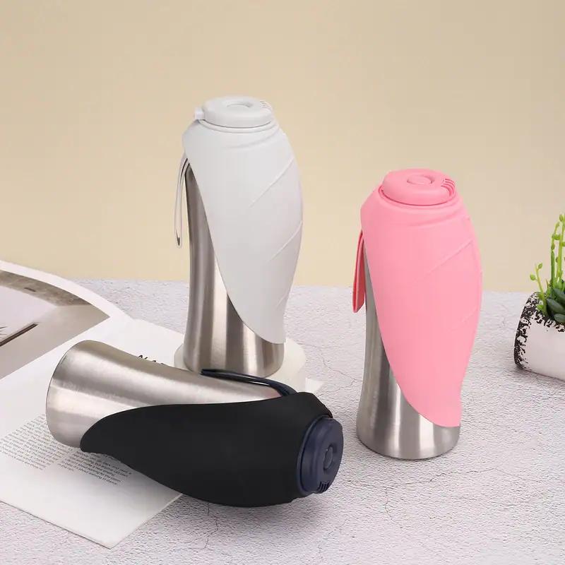 Two stainless steel travel mugs with silicone sleeves, one pink and one white, on a light-colored surface with a plant in the background.