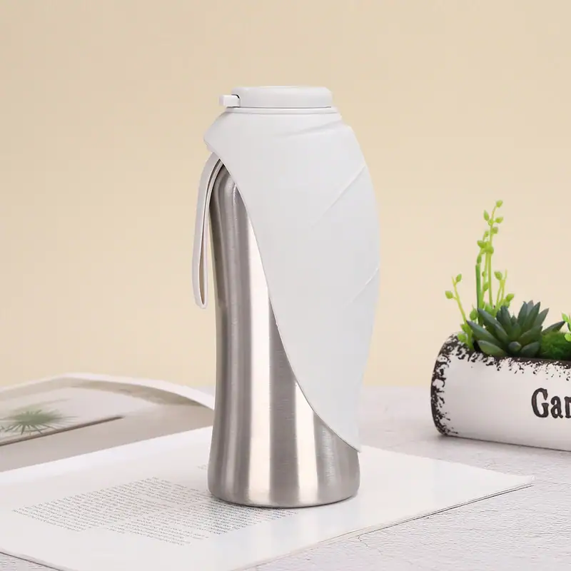 Stainless steel travel mug with white silicone sleeve and lid, designed for hot and cold beverages, on a white surface with a plant in the background.