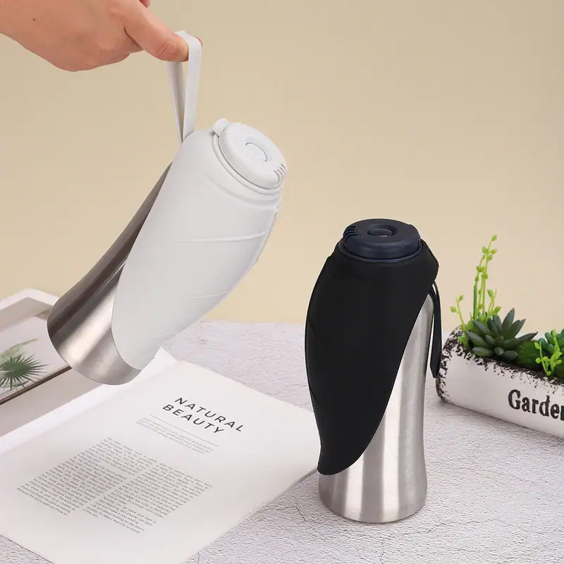 Two portable thermos flasks, one white and one black, on a table with a plant and a magazine, ideal for travel and outdoor use.
