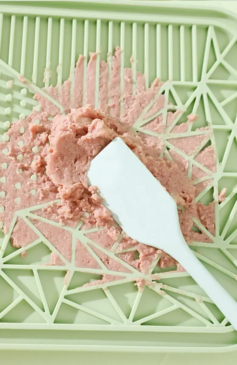 Close-up of pink ice cream with a white spatula in a light green basket, showcasing a smooth texture and appealing presentation.