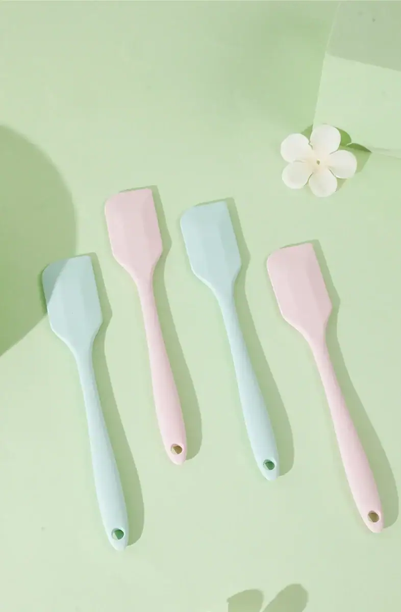 Set of four pastel-colored silicone spatulas in pink, blue, and green on a light green background, ideal for kitchen use and cooking.