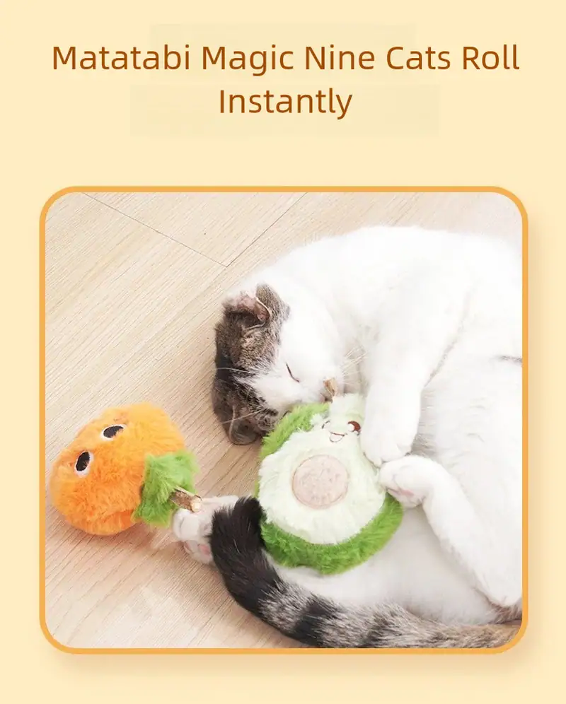 Cute cat playing with Matatabi Magic Nine Cats Roll toy, lying on wooden floor, with orange and green plush toys nearby.