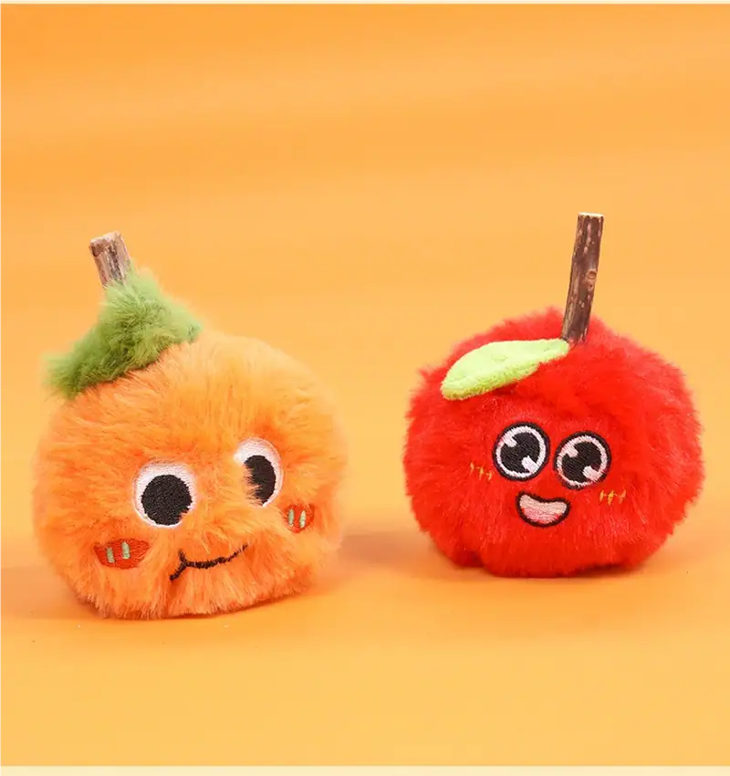 Two adorable plush fruit toys with expressive faces, one resembling an orange with a green stem and the other a red apple with a leaf, on a yellow background.